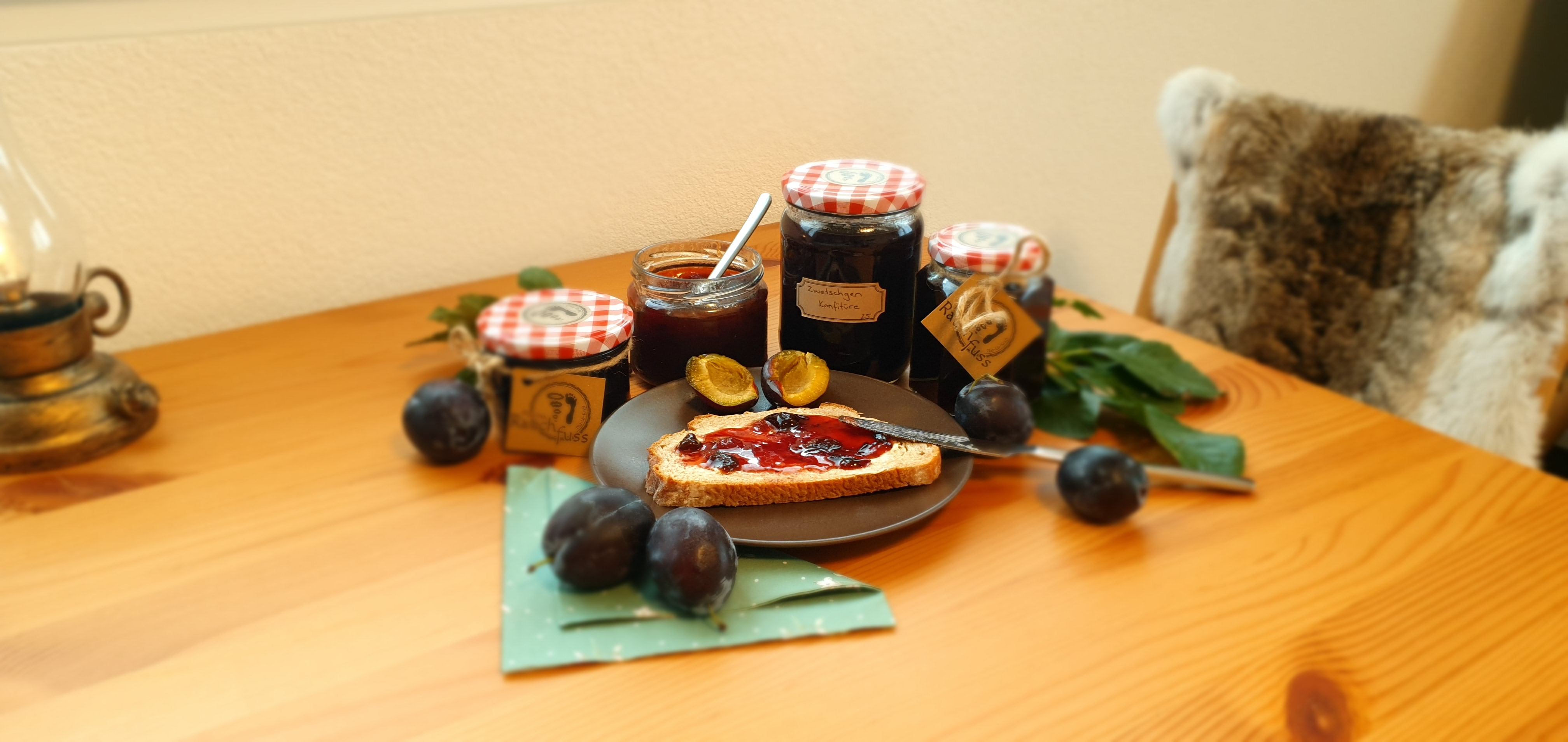 Ein Holztisch mit 4 verschiedenen grössen von Einmachgläsern, ein Teller mit einem Brombeerkonfitürebrot und dekoriet mit frischen Brombeeren und deren Blätter